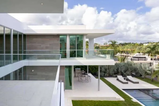 Modern two-story home with floor-to-ceiling glass, a glass-railed upper terrace and an outdoor dining area beside a pool
