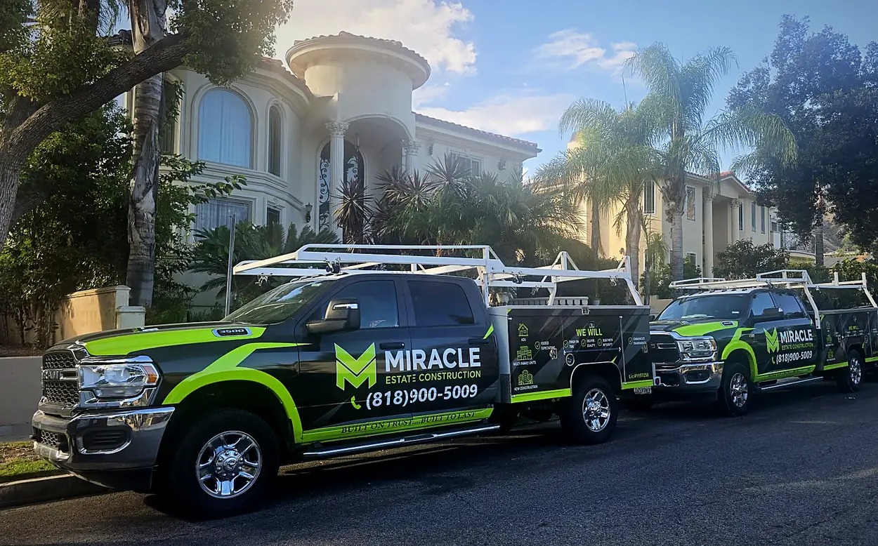 Two Miracle Estate Construction work trucks parked on a residential street in front of a large stucco home