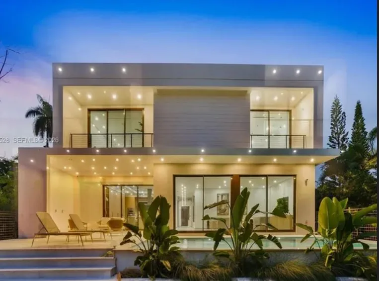 Rear of a modern two-story home at dusk with large sliding glass doors, upper balconies, a covered terrace and a pool