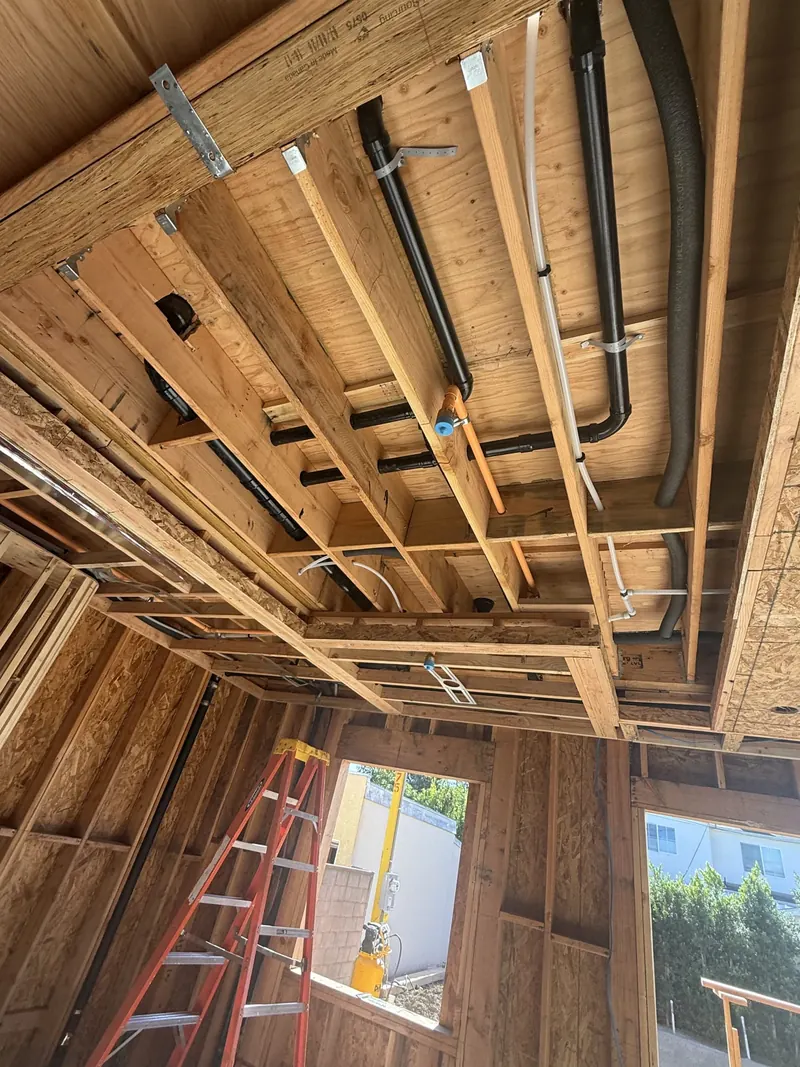 Interior view of exposed wood framing with ductwork, a ladder and window openings in an ADU under construction