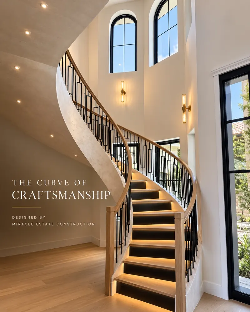 Curved staircase with a black metal railing, lit treads and tall arched windows in a new home