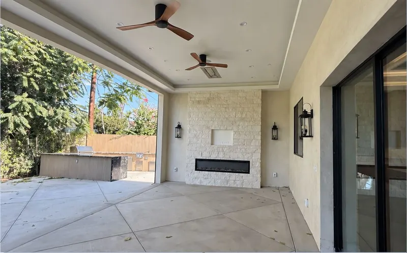 Covered patio with ceiling fans, a stone wall with a linear fireplace and large sliding glass doors