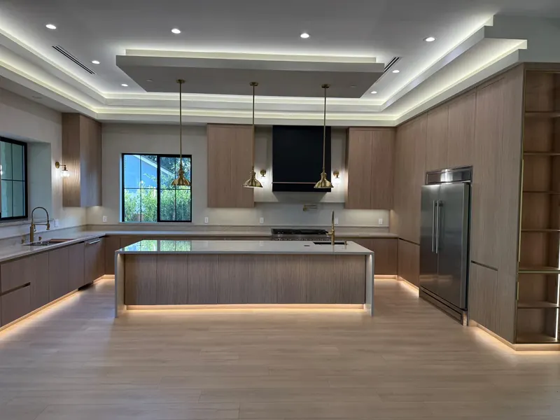 Modern kitchen with flat-panel wood cabinets, a large stone island, pendant lights and a recessed ceiling with indirect lighting