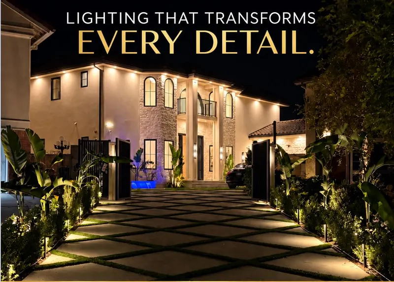 Two-story house at night with a lit arched entry, uplit planting and a diamond-pattern paver walkway