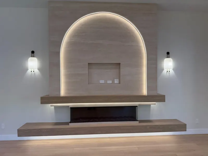 Living room feature wall with an arched indirect-lit recess, wall sconces and a floating wood hearth with a linear fireplace