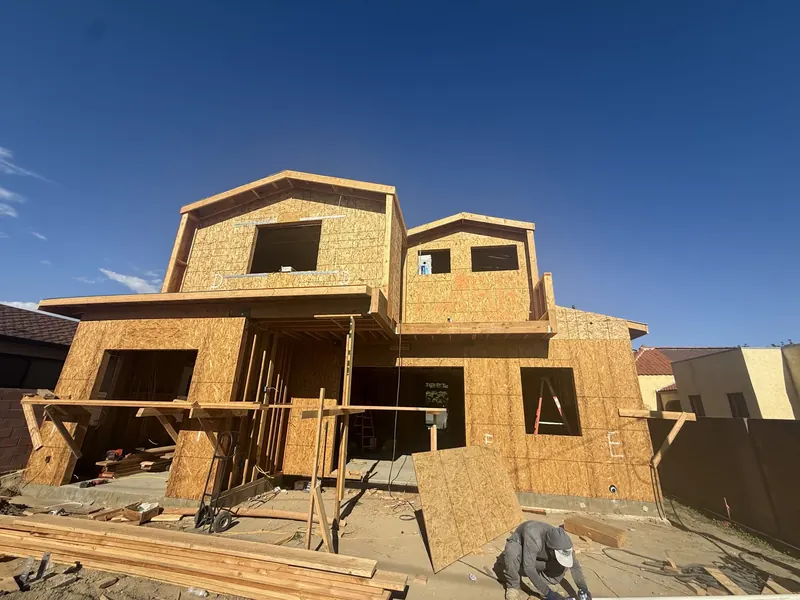 Two-story house framed in plywood sheathing against a blue sky with a worker on site